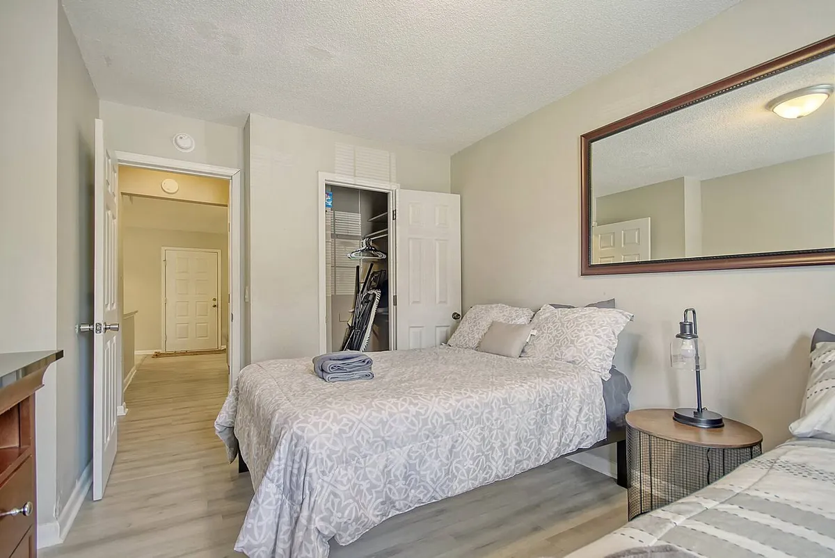 This image features beds with cozy linens, a mirror, a reading lamp, and a closet, all arranged in a softly lit, peaceful space. The scene invites quiet relaxation, reading, or gentle conversation.