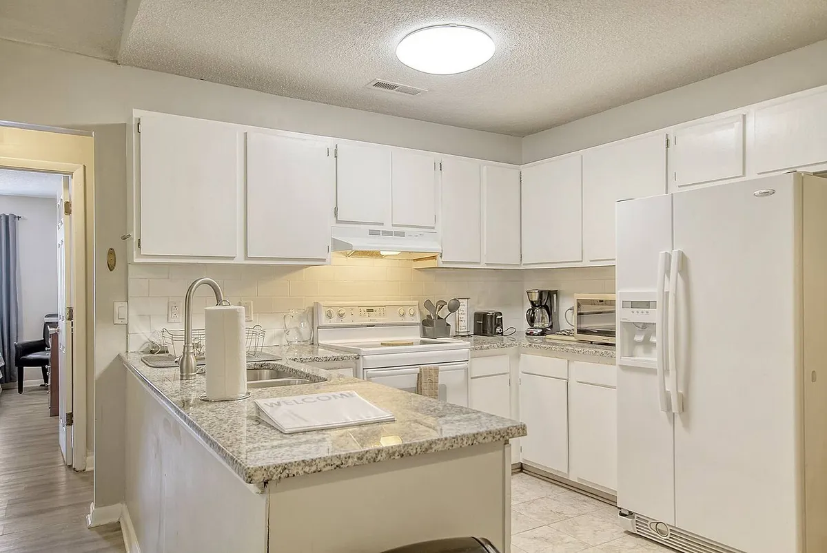 A welcoming kitchen scene featuring granite countertops, white cabinetry, modern appliances, and a coffee maker. The kitchen is accessible and open, capturing the flow of the main living areas.