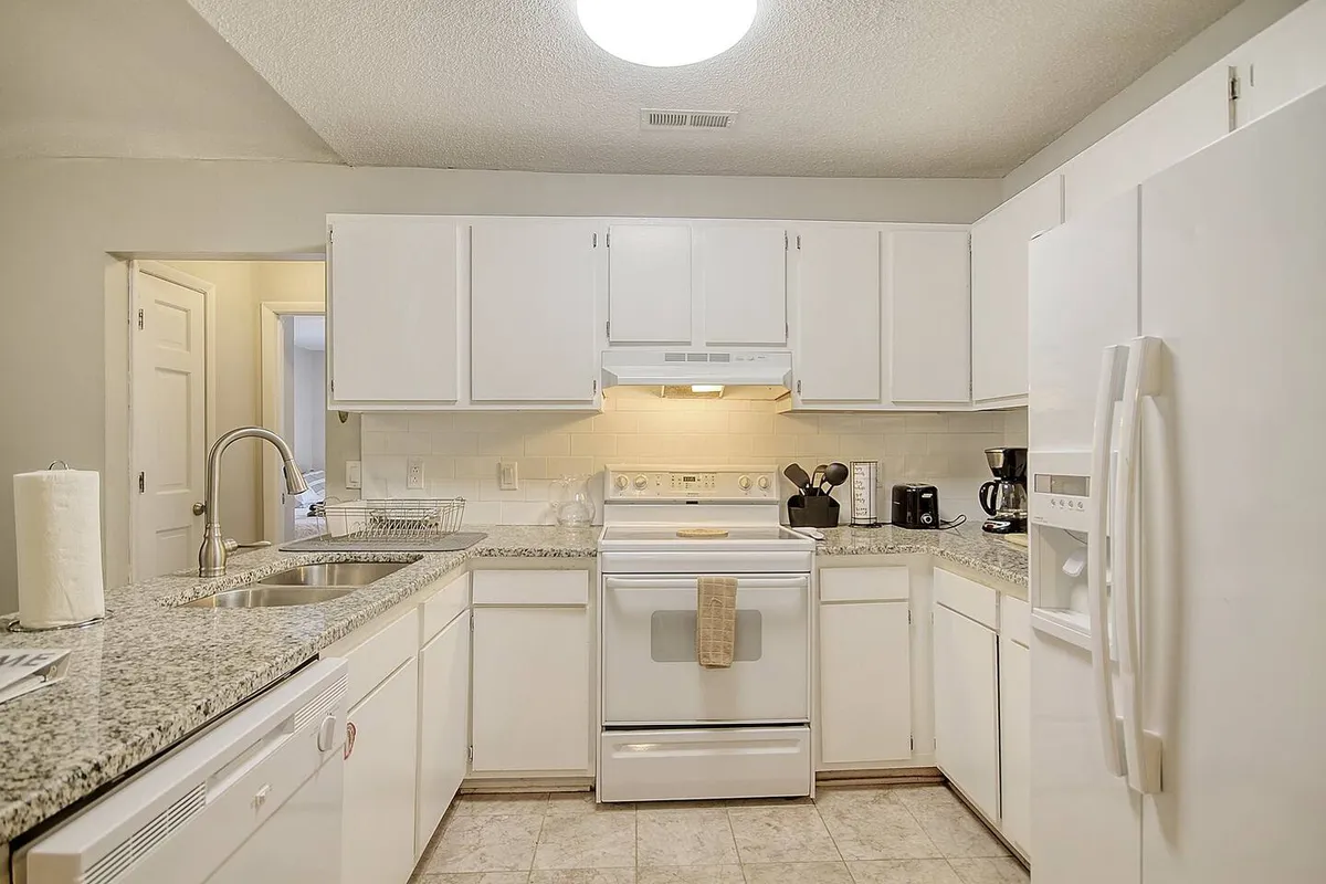 A bright, welcoming kitchen featuring granite countertops, crisp white cabinetry, and essential appliances. The countertop space is generous, making it easy to prepare meals and gather for cooking activities. The overall layout is open and inviting, ideal for collaborative meal prep and casual conversation.