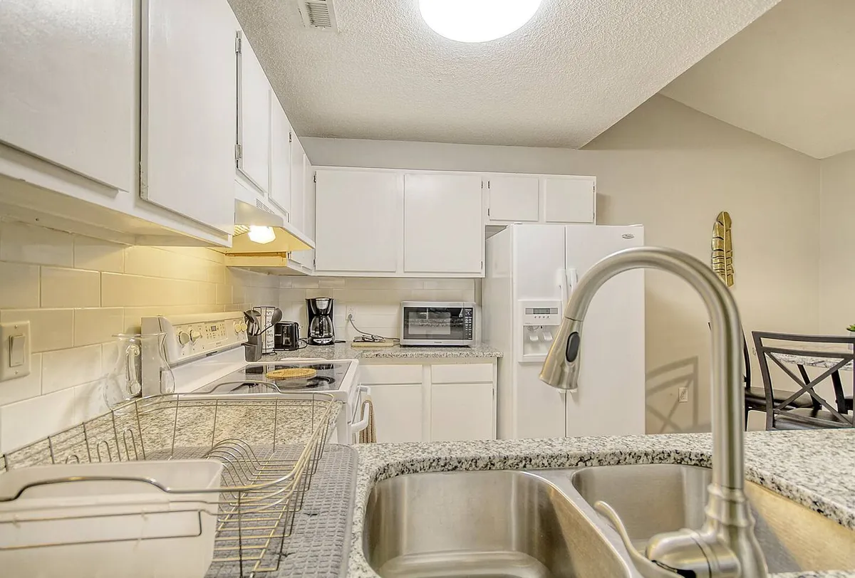 A modern kitchen scene featuring granite countertops, white cabinetry, stainless steel appliances, and a sink. The space looks clean, functional, and well-organized, offering all the amenities needed for cooking and entertaining. Its open design encourages interaction while preparing meals.