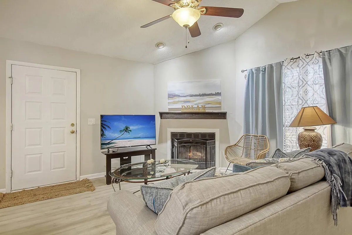 A comfortable living area with a plush sofa, a television displaying a tranquil beach scene, and a fireplace. The space is further adorned with a decorative lamp and elegant curtains, creating a cozy, serene environment ideal for unwinding, reading, or enjoying time with friends and family.
